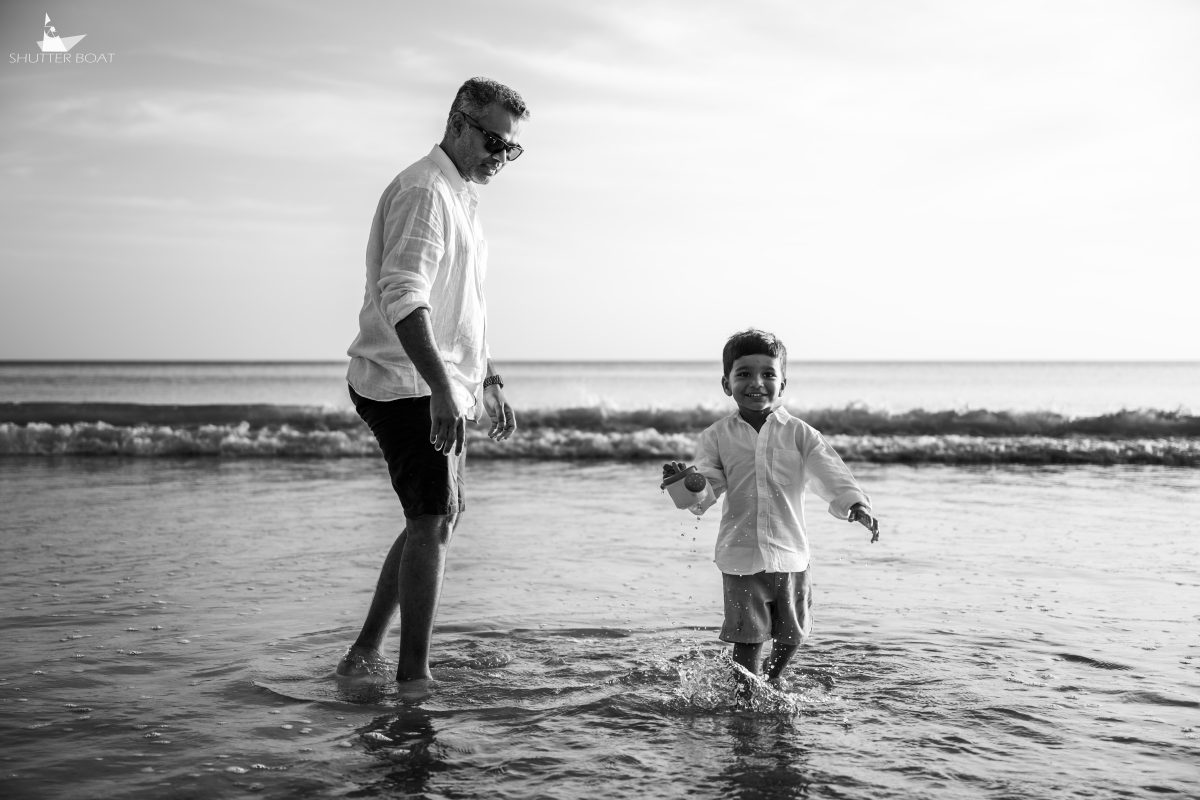 Black and white photo of a father walking in the shallows with his young son