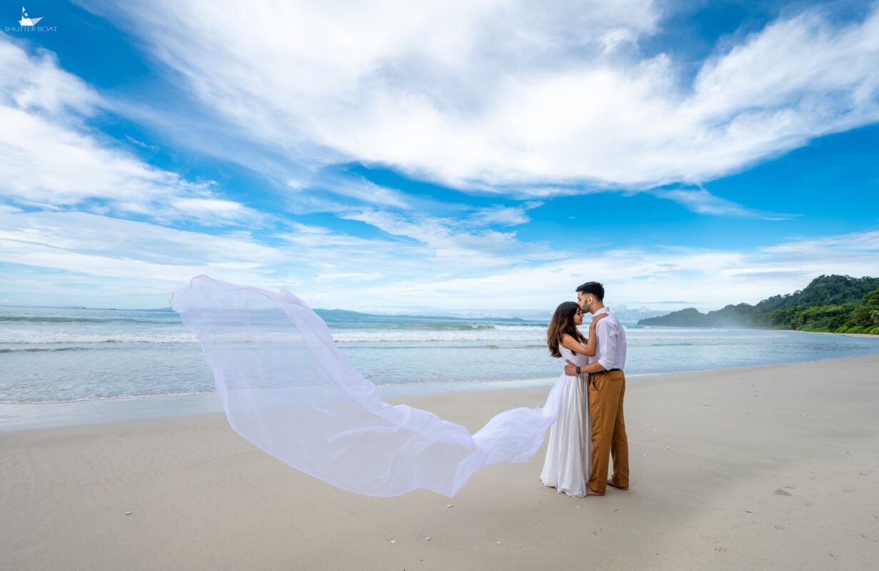 Couple embracing on the beach with a white veil flowing beside them