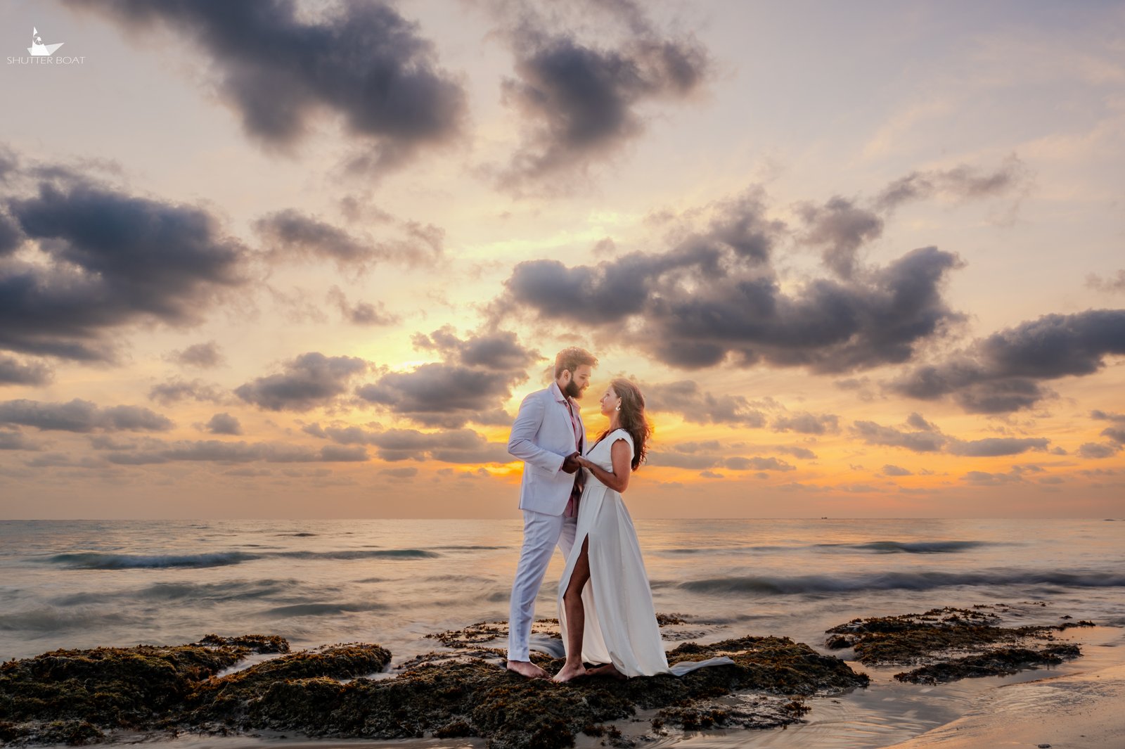 Couple in white at sunset on the rocky shore
