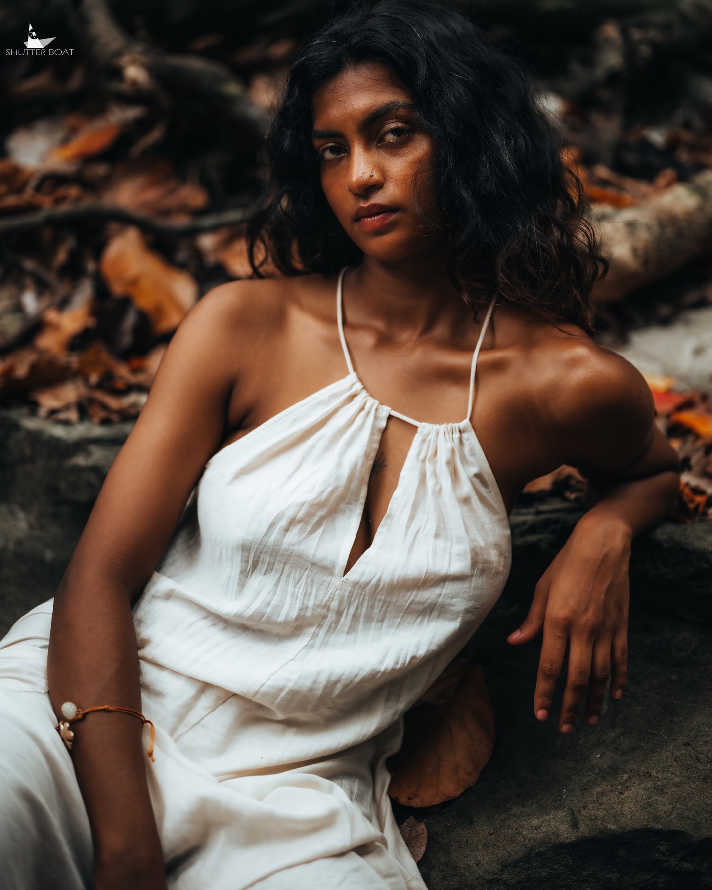 Woman in a white dress seated beside forest rocks