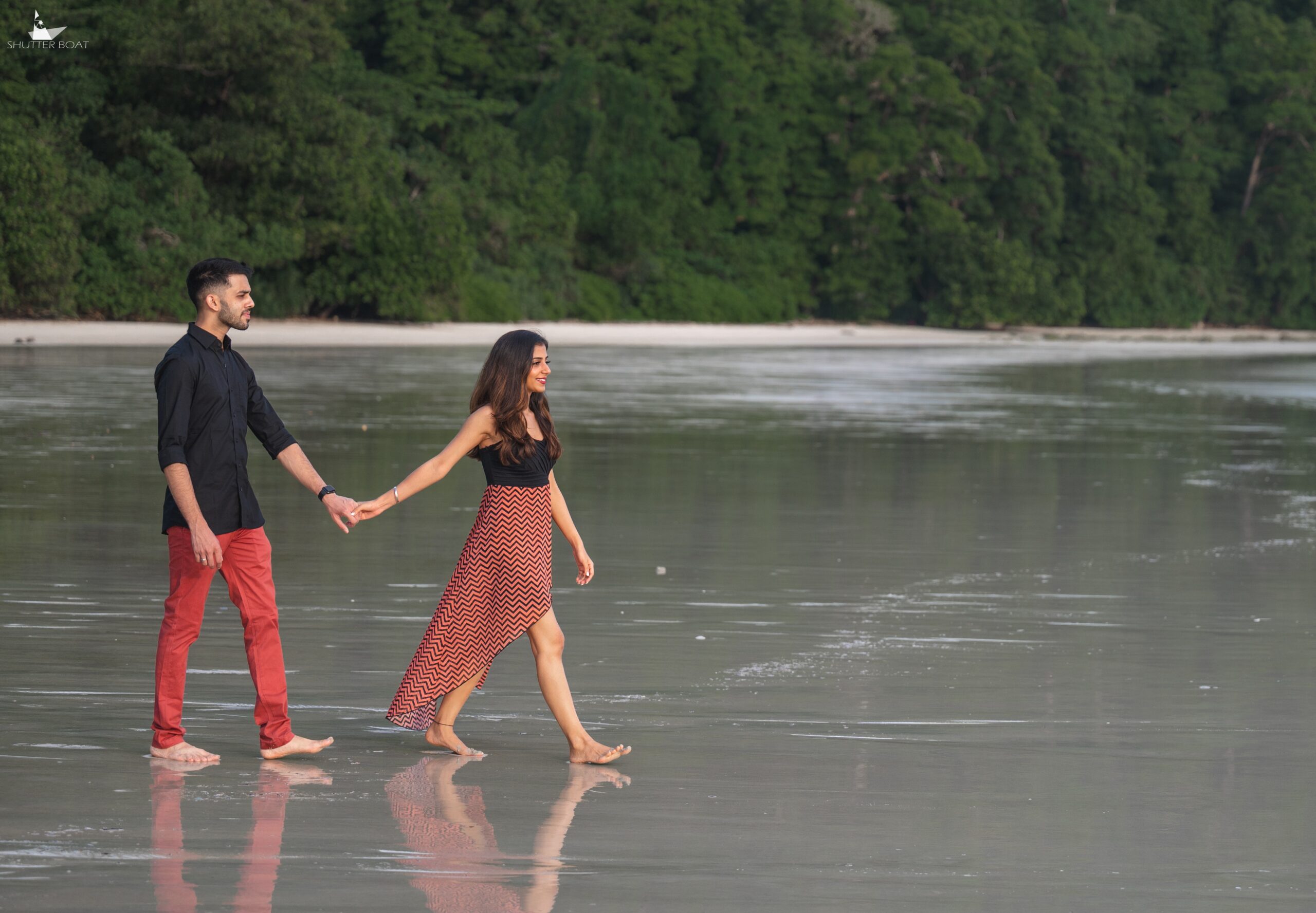 Couple walking across wet sand with reflections