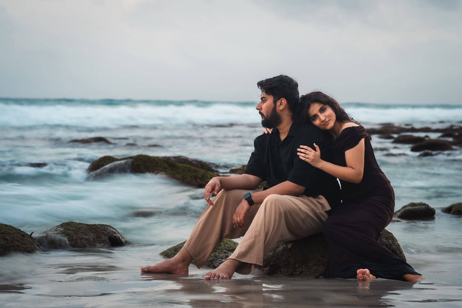 Couple seated together on rocks by the sea
