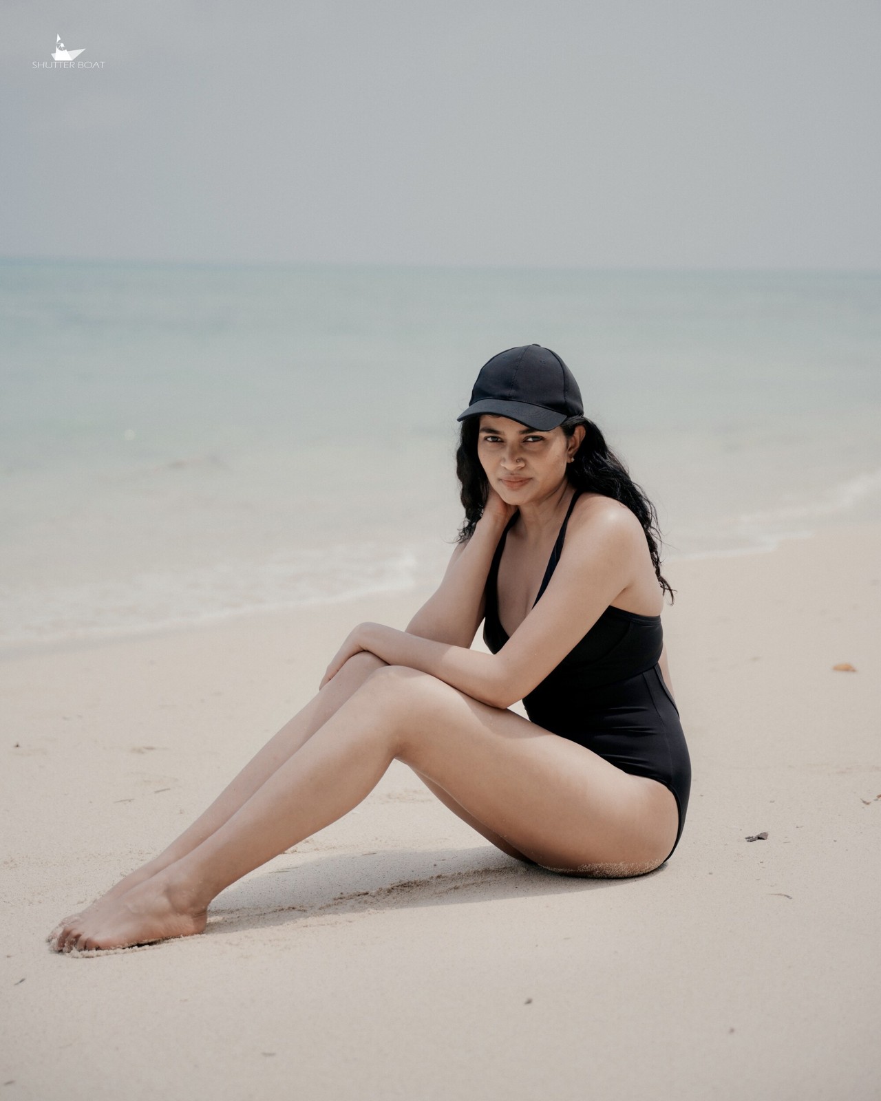 Woman in a black swimsuit and cap seated on the sand beside the sea